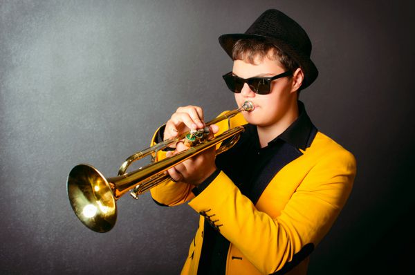 نوازنده خوش تیپ جاز تی پت با کلاه ژاکت زرد و عینک مشکی پرتره نوازنده جوان tpet در استودیو