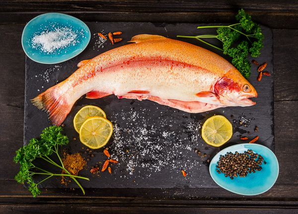 ماهی قزل آلای رنگین کمان تازه با ادویه روی میز چوبی تیره آماده سازی