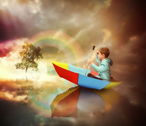 کودک کوچکی در یک قایق چتری نشسته است و با رنگین کمان به درخت نوری دوردست نگاه می کند تا مفهومی تخیل یا آزادی داشته باشد