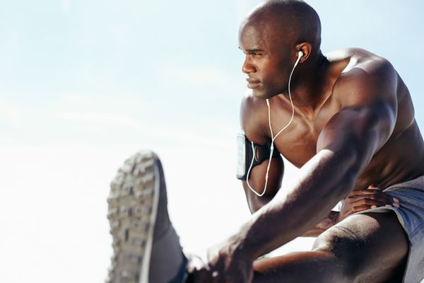 تصویری از مرد جوان عضلانی که در مقابل آسمان تمرین می کند مرد آفریقایی با دراز کردن پای خود به دور نگاه می کند مدل مردانه بدون پیراهن در حال ورزش در فضای باز