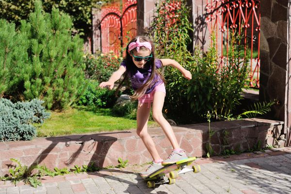 دختر بچه مدرسه ای ناز سوار اسکیت بورد در پارک