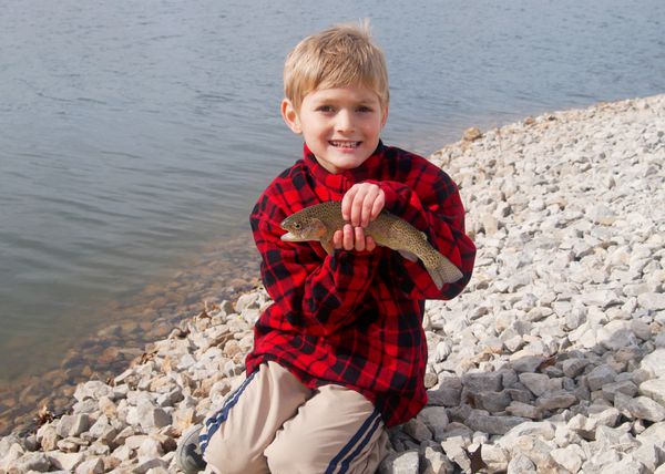 پسر شاد و ماهی قزل آلای رنگین کمانی که در حال ماهیگیری در دریاچه است