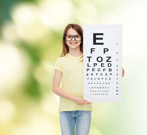 مفهوم بینایی سلامتی و مردم - دختر کوچک خندان با عینک با نمودار چک کردن چشم