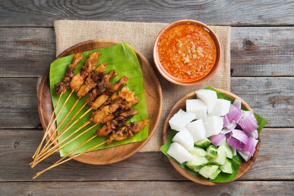 نمای بالای سر مرغ ساتای مالزیایی با سس بادام زمینی خوشمزه کتوپات پیاز و خیار روی میز ناهار خوری چوبی یکی از غذاهای معروف محلی است