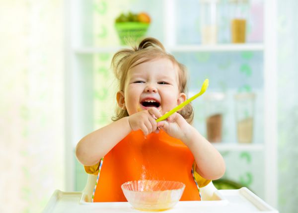 کودک بامزه در حال خوردن غذای سالم در آشپزخانه