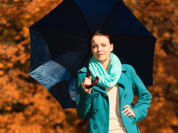 شادی آزادی و مفهوم مردم دختر نوجوان زن جوان در حال قدم زدن با چتر آبی در پارک پاییزی در فضای باز