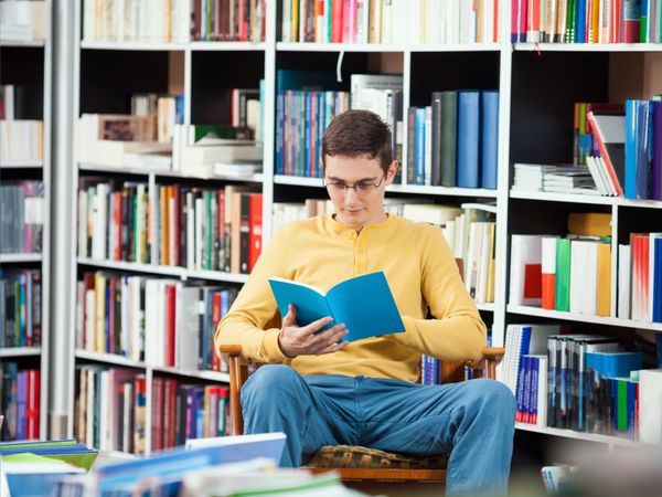 مرد جوانی در کتابخانه نشسته و مشغول خواندن کتاب است