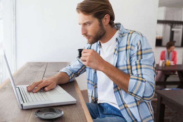 مرد مورد استفاده از لپ تاپ در حال نوشیدن اسپرسو در کافی شاپ