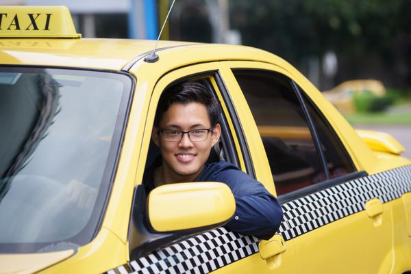 پرتره راننده تاکسی چینی خوشحال در ماشین زرد که لبخند می زند و به دوربین نگاه می کند