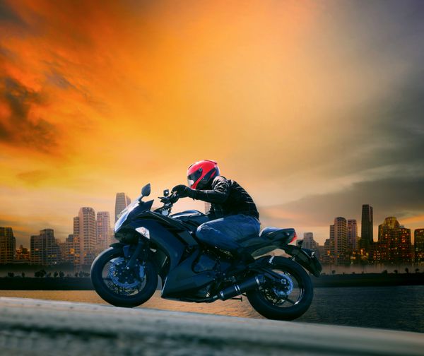 مرد جوان و لباس ایمنی سوار بر موتور سیکلت بزرگ در برابر آسمان تاریک و صحنه شهری زیبا با کپی sp