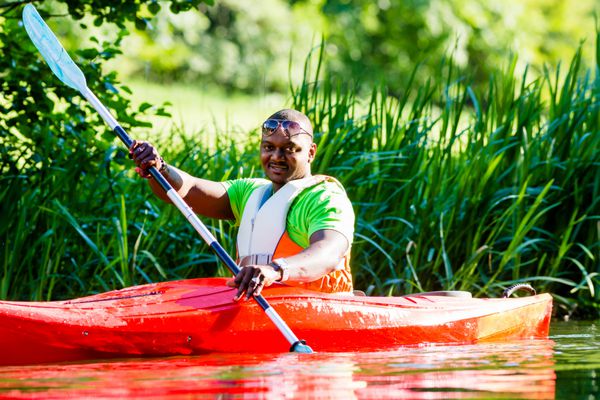 مرد آفریقایی در حال پارو زدن با قایق رانی در رودخانه جنگلی