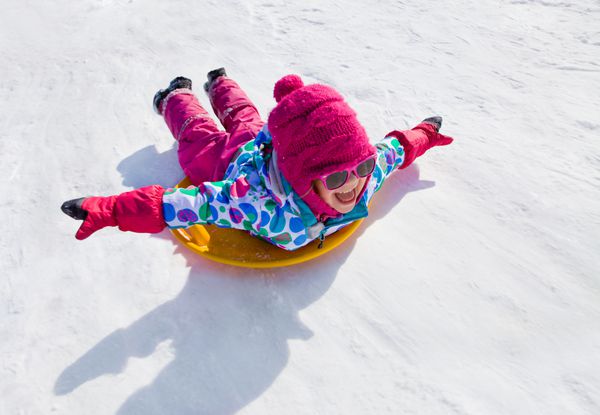 دختر بچه سوار بر سرسره های برفی در زمستان