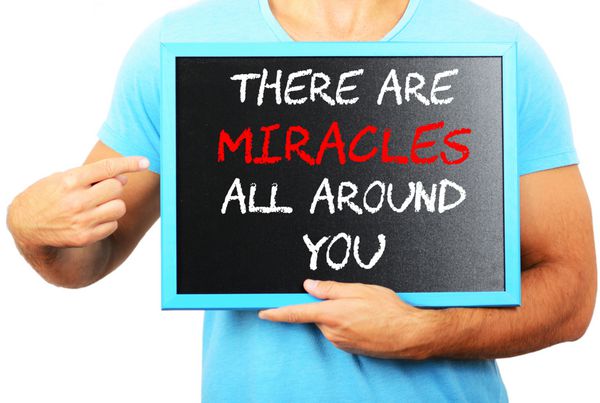 مردی که تخته سیاه را در دست گرفته و به این کلمه اشاره می کند که معجزه هایی در اطراف شما وجود دارد