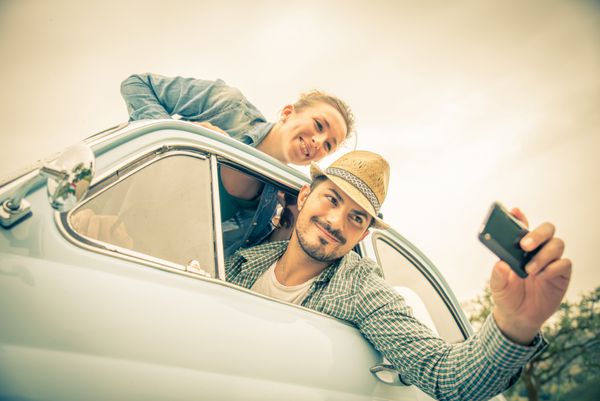 زوج شاد در ماشین قدیمی - دو دوست در حال عکسبرداری در یک سفر جاده ای - مفاهیم زوج مسافرت و سرگرمی