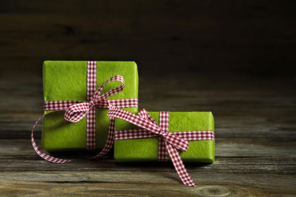دو هدیه سبز با روبان شطرنجی قرمز سفید در زمینه چوبی