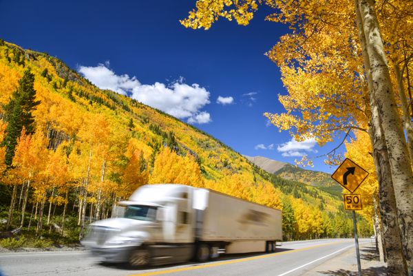کامیون تریلر تراکتوری که در امتداد بزرگراه کلرادو در روز رنگارنگ پاییزی رانندگی می کند