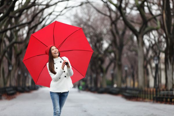 زن با چتر قرمز در حال قدم زدن در پارک در پاییز دختر چند نژادی خندان و شاد با چتر قرمز در پارک مرکزی منهتن شهر نیویورک ایالات متحده آمریکا راه می‌رود
