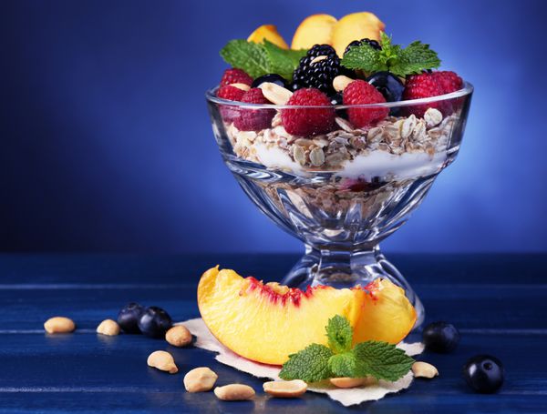صبحانه سالم - ماست با میوه های تازه انواع توت ها و موسلی در کاسه ای شیشه ای روی میز چوبی رنگی در زمینه رنگی تیره سرو می شود