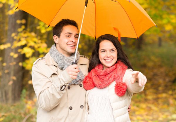 مفهوم عشق رابطه فصل خانواده و افراد - زوج خندان با چتر در حال قدم زدن در پارک پاییز