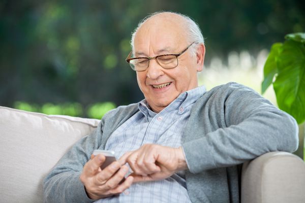 پیامک مرد سالمند خندان از طریق تلفن همراه در ایوان خانه سالمندان