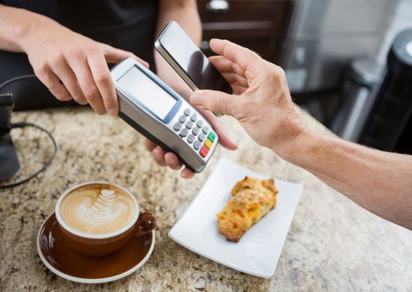تصویر برش خورده مشتری در حال پرداخت از طریق تلفن همراه از طریق خواننده الکترونیکی در پیشخوان کافه