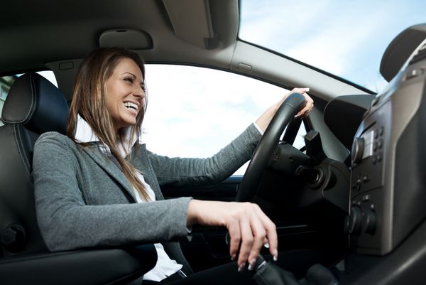 زن جوان جذاب رانندگی می کند چوب دنده را در دست گرفته و لبخند می زند