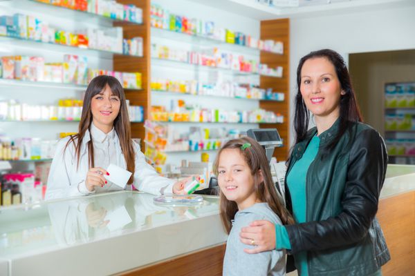 داروساز شاد زن شیمیدان به دختر بچه در داروخانه داروخانه ویتامین می دهد تمرکز انتخابی