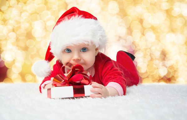 نوزاد کوچک زیبا کریسمس را جشن می گیرد تعطیلات سال نو کودک در لباس کریسمس با هدیه