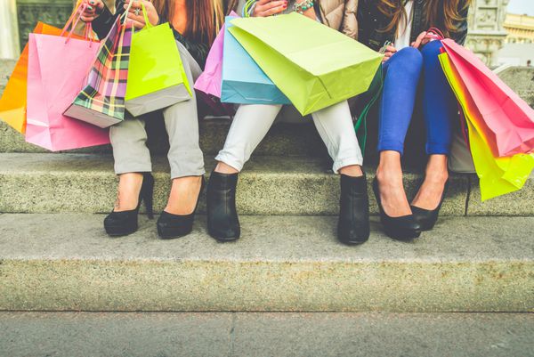 زنان با کفش‌های پاشنه بلند و کیف خرید - سه دختر روی پله‌ها نشسته‌اند و بعد از خرید هدایا صحبت می‌کنند