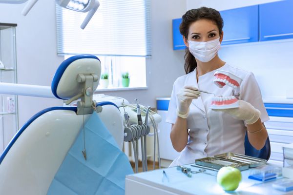 زن دندانپزشک با ماسک در مطب دندان شناسی سیب سبز در دست دارد مفهوم مراقبت های بهداشتی