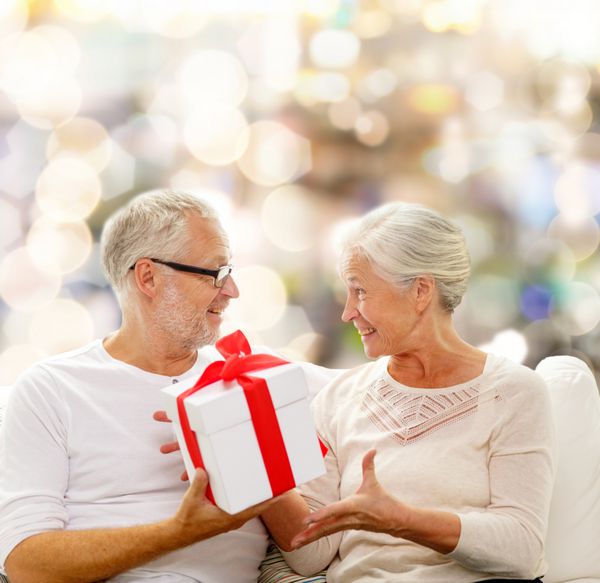 خانواده تعطیلات کریسمس سن و مفهوم افراد - زوج سالمند شاد با جعبه هدیه روی پس زمینه چراغ ها