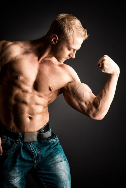 مرد بدنساز عضلانی که روی پس زمینه تیره ژست گرفته است زیبایی مردانه ورزش ها