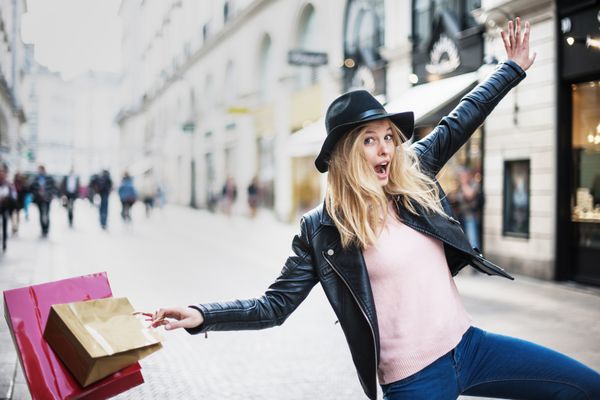 یک زن جوان شیک پوش که در شهر مشغول خرید است خوشحالی خود را از پریدن و خندیدن ابراز می کند