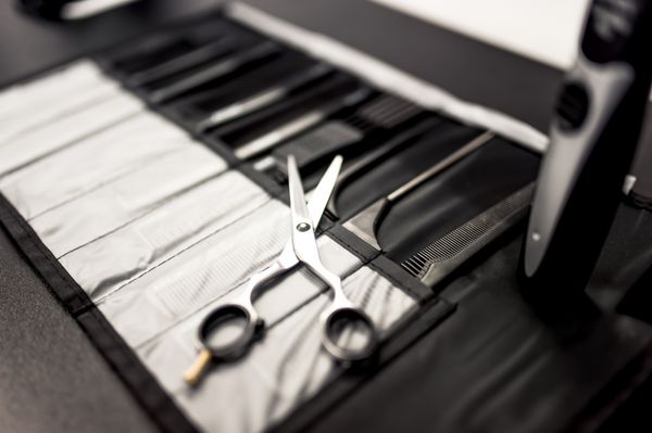 ابزار آرایشگری حرفه ای روی میز با قیچی و شانه های مشکی از نمای نزدیک
