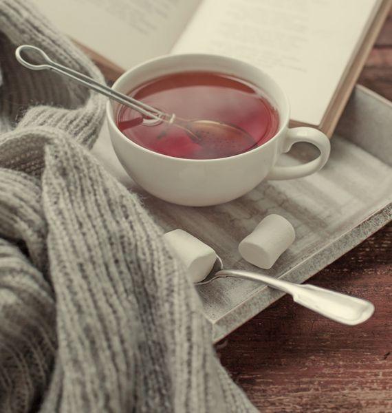 ژاکت بافتنی گرم فنجان چای و کتاب روی یک سینی چوبی