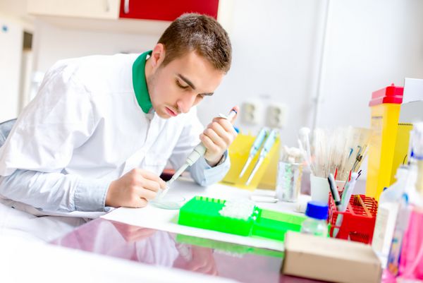 دانشمند و شیمیدان جوان خوش تیپ در حال بررسی نمونه ها و عناصر شیمیایی برای بیماری ها در آزمایشگاه ویژه