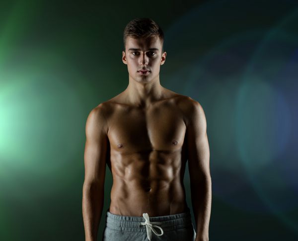 ورزش بدنسازی قدرت و مفهوم افراد - مرد جوان با نیم تنه ای عضلانی که روی پس زمینه تاریک ایستاده است