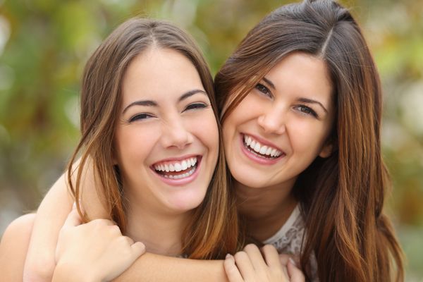 دو دوست زن در حال خندیدن با دندان های سفید عالی با پس زمینه سبز