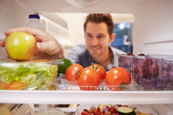 مردی که به داخل یخچال پر از غذا نگاه می کند و سیب را انتخاب می کند