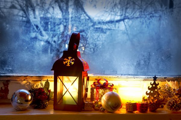 فانوس گرم روی پنجره یخ زده با تزئینات شمع و کریسمس محیطی دنج