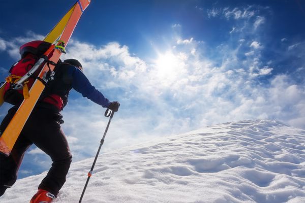 کوهنورد اسکی در حال راه رفتن در امتداد خط الراس برفی شیب دار با اسکی در کوله پشتی در پس زمینه یک آسمان دراماتیک مفاهیم ماجراجویی موفقیت شجاعت عزم ورزش شدید