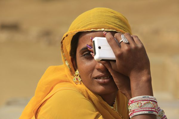 جیسالمر هند - 9 نوامبر 2014 زن هندی ناشناس نشسته و یک تلفن همراه در دست دارد