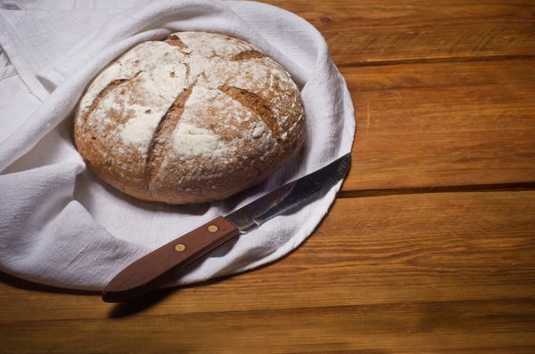 نان گلگون پیچیده شده در حوله کتان سفید روی میز چوبی