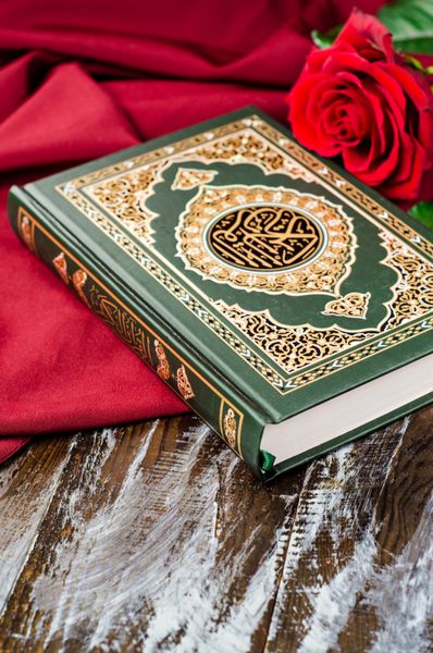 قرآن - کتاب مقدس اسلام با گل رز و روسری قرمز در زمینه چوبی تمرکز انتخابی