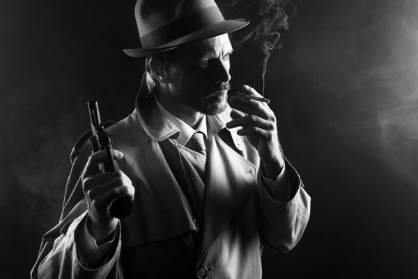 فیلم نوآر گانگستر جذاب با مانتو در حال کشیدن سیگار و هفت تیر در دست
