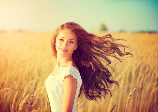 دختر زیبایی در فضای باز که از طبیعت لذت می برد دختر مدل نوجوان زیبا با موهای بلند و سالم دمیدن در زمین بهار نور خورشید درخشش خورشید زن شاد رایگان رنگ آمیزی شده در رنگ های گرم