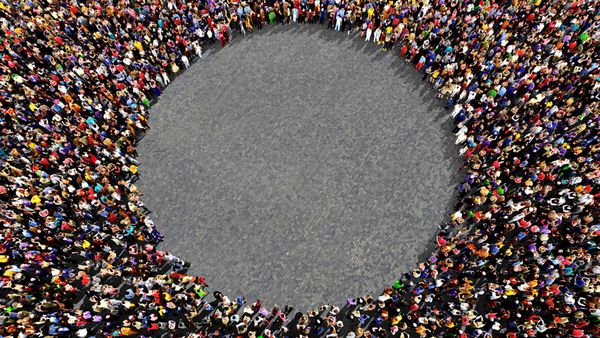 گروه بزرگی از مردم که از بالا دیده می‌شوند به شکل دایره جمع شده‌اند و روی پس‌زمینه پیاده‌روی خیابان ایستاده‌اند - فرمت منظره گسترده