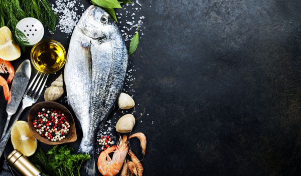 ماهی تازه خوشمزه در پس زمینه پرنعمت تیره ماهی با گیاهان معطر ادویه جات و سبزیجات - غذای سالم رژیم غذایی یا مفهوم آشپزی