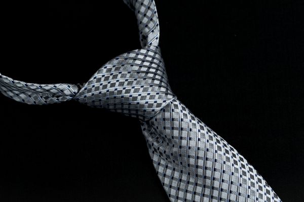 جزئیات یک گره ویندسور روی کراوات گره دار خاکستری و آبی جدا شده در برابر پس زمینه سیاه