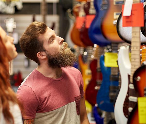 موسیقی فروش مردم مفاهیم موسیقی و مفهوم سرگرمی - زوج شادی از نوازندگان که گیتار را در فروشگاه موسیقی انتخاب می کنند